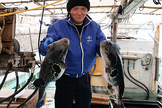 船の上で両手に２キロはあるトラフグを持っている中島豊さんの画像