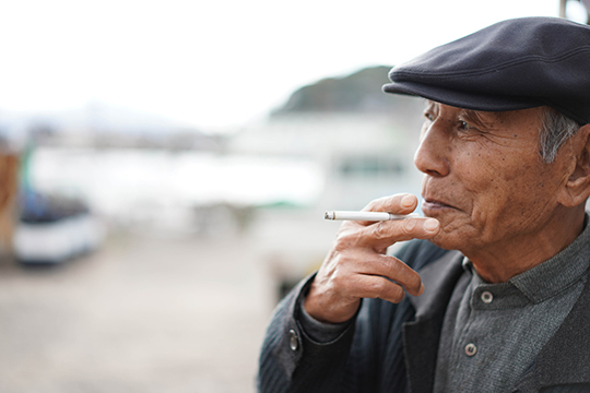 港をバックにタバコを手にしている泉良英さんのアップの画像