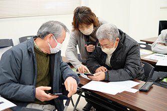 桑原先生が生産者さん二人にスマホ操作を教えている画像