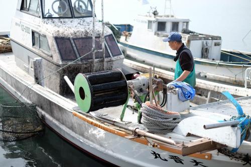 操舵室のガラスがイカ墨で黒くなっている大晋丸の上に立つ梅野孝昭さんの画像