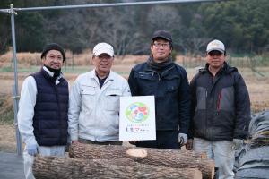 シイタケの原木の後ろに立つ安永敏雄さんと3人の社員の皆さんの画像